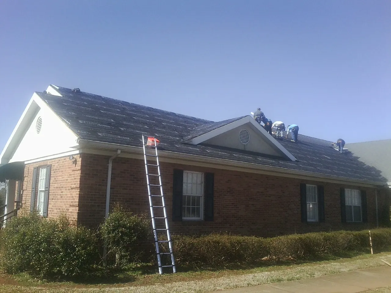 Crew tearing shingles off a brick ranch roof with a ladder set — Emergency Roof Repair work by our crew in West Hartland