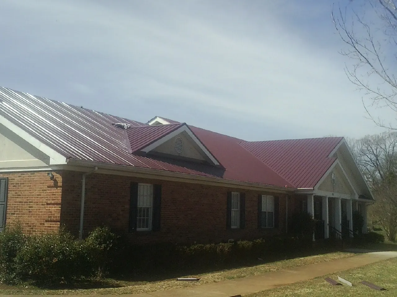 Red metal roof with gabled entries on a long brick building, from a Hail Damage Roof Repair job in West Hartland