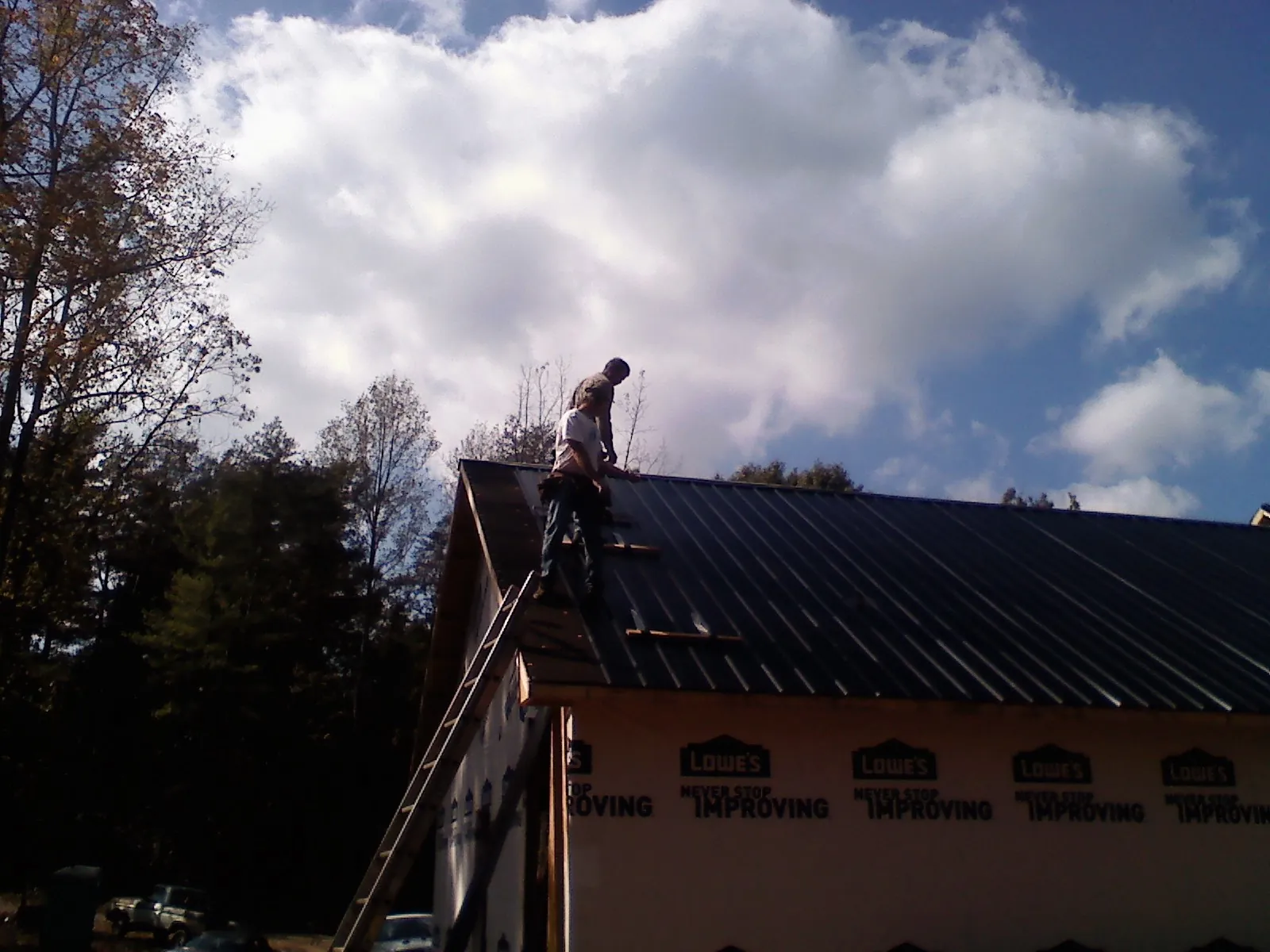 Roofer fastening dark metal panels high against a cloudy sky, from a Roof Inspection job in West Hartland