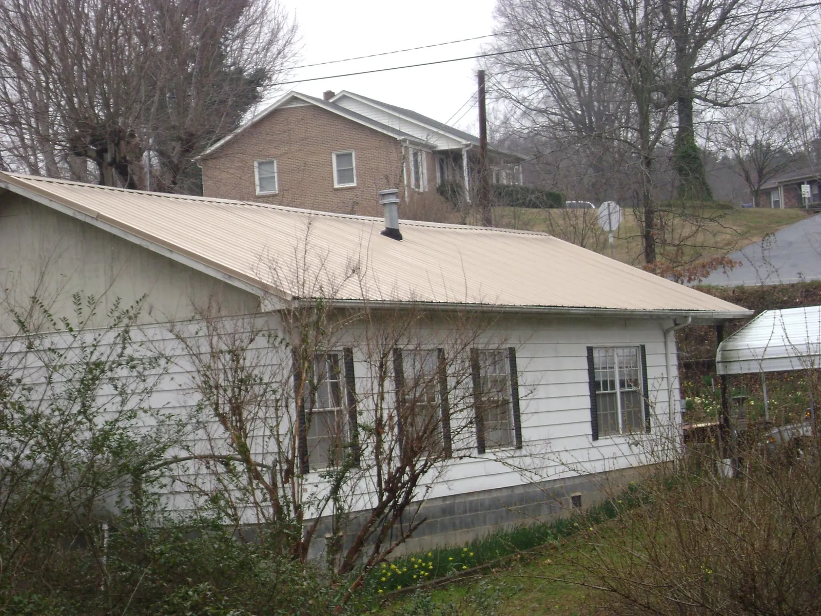 Tan metal roof on a white sided house set into a hillside — Commercial Roofing by Roofing Brothers in West Hartland