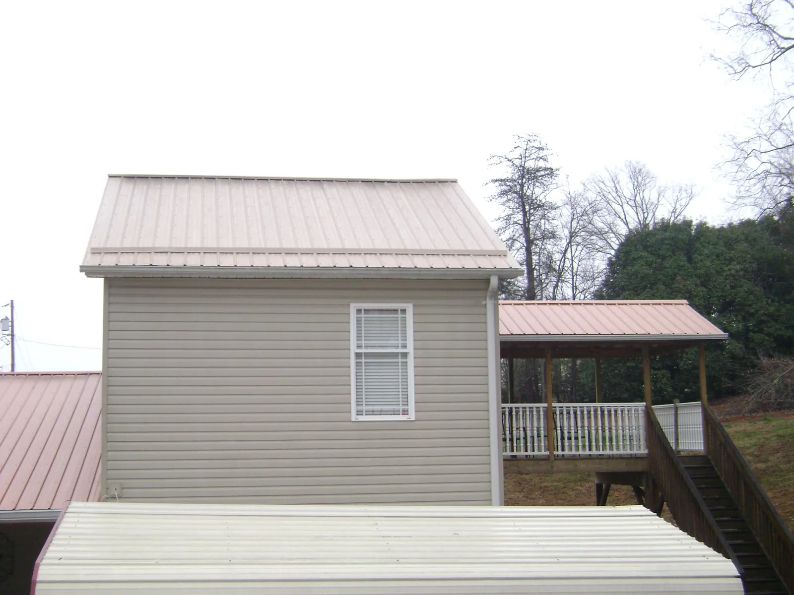 Tan metal roofs on a two story addition and attached porch, from a Roof Replacement job in West Hartland